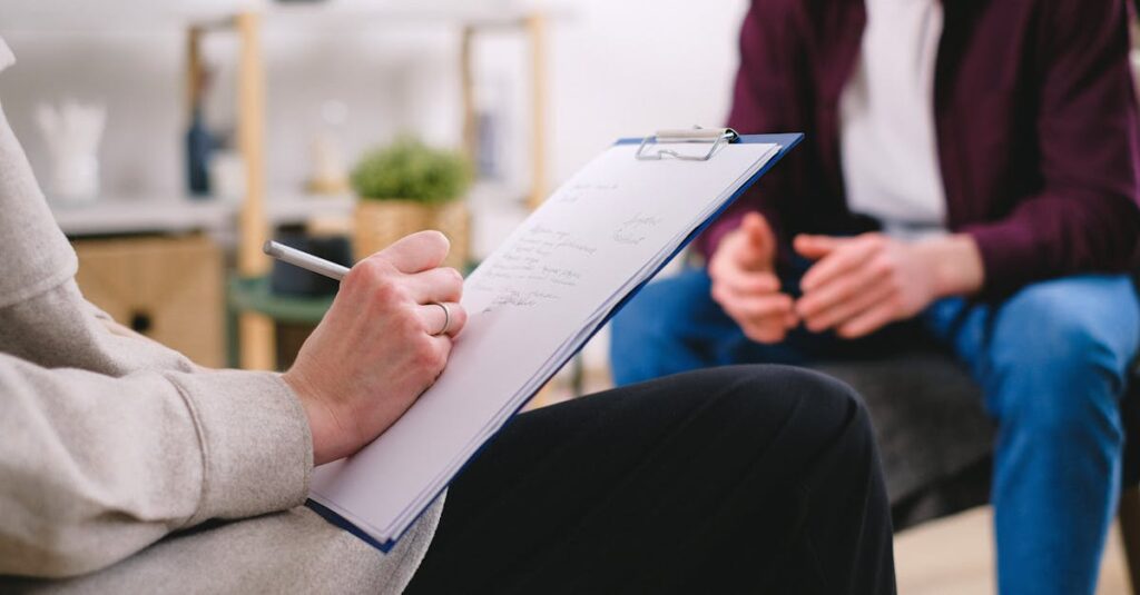Close-up of a therapist writing notes on a clipboard while conversing with a patient.